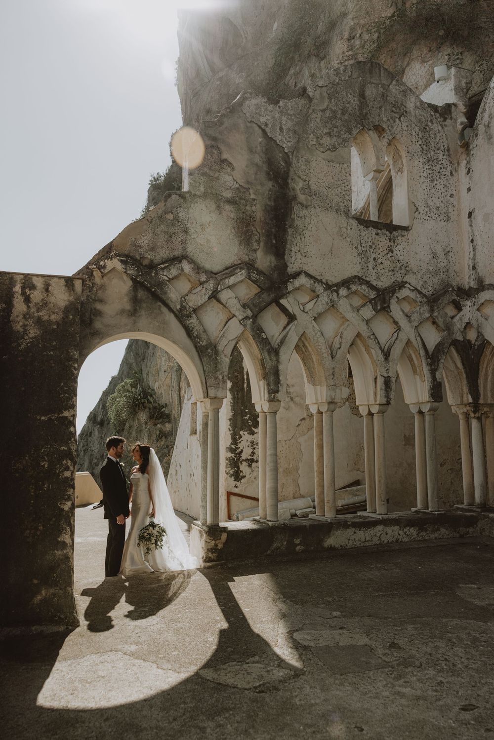 A wedding couple silhouetted in gothic stone archways with dramatic lighting.