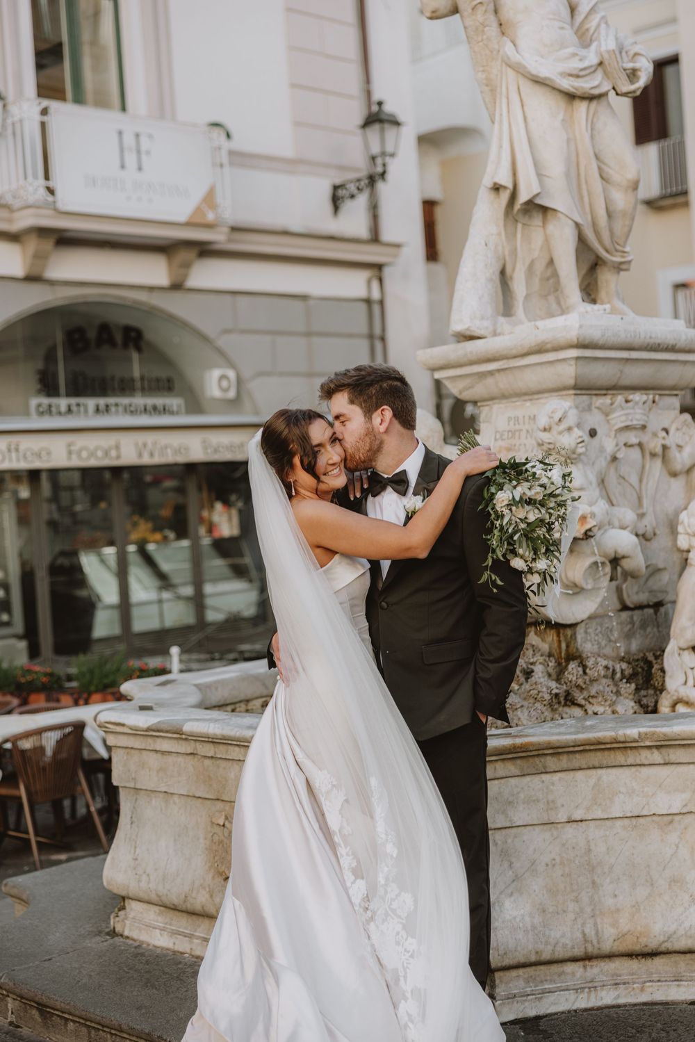 A romantic wedding moment captured beside a classical statue and fountain.