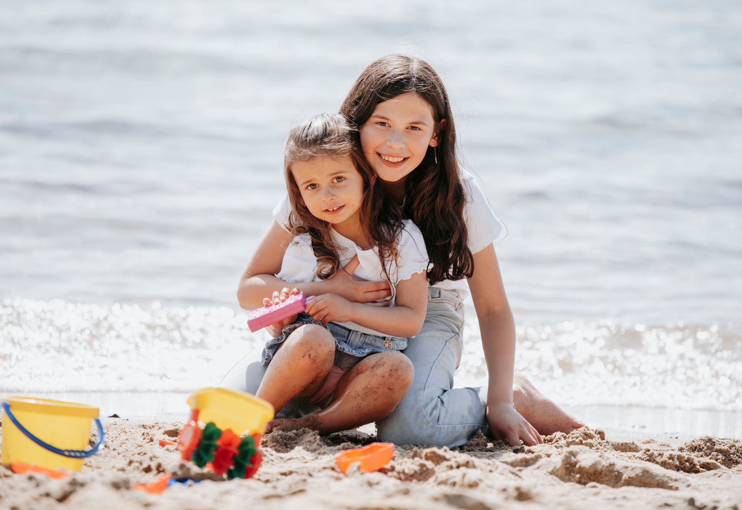 Mother and daughter playing together on a sandy beach near the ocean on a sunny day.