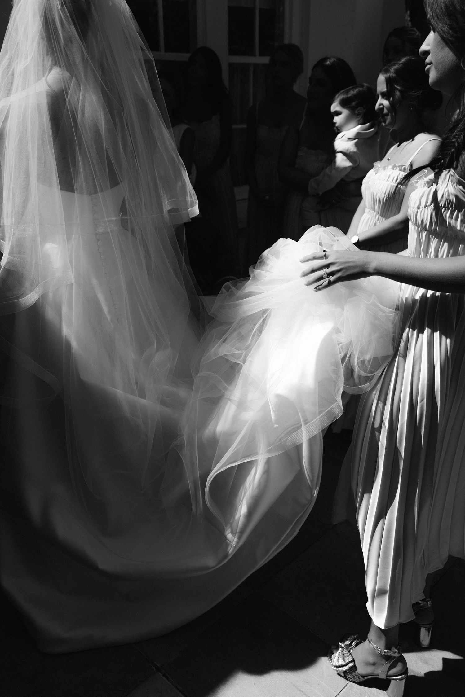 A black and white image showing the flowing layers of a wedding dress and veil being adjusted.