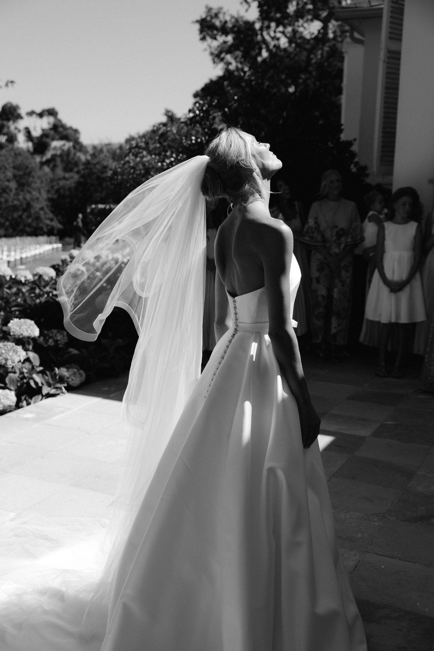 A bride in a flowing white wedding gown and veil twirls gracefully in an outdoor setting.