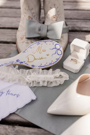 White bridal shoes and garter arranged on weathered wooden planks with decorative text details.