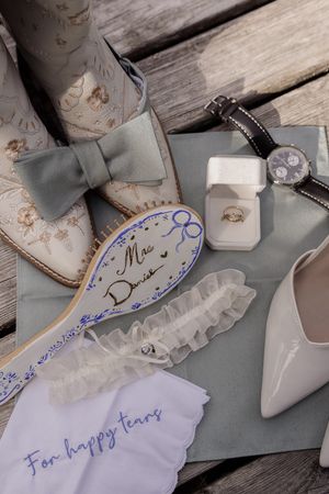 White bridal garter with blue embroidery details laid out on wooden surface.