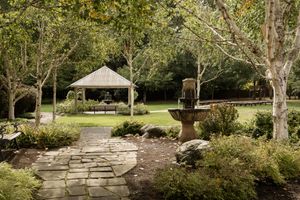 A serene garden pathway lined with mature trees and stone walls on a sunny day.