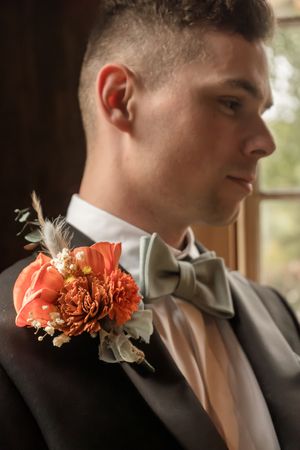 Close-up of coral boutonniere on groom's lapel in formal wedding attire.