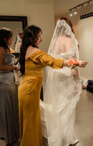 Wedding preparation scene with attendants helping adjust a bride's flowing white veil and dress.