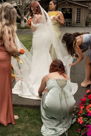 Wedding party members in dusty rose dresses gather around a bride in a white gown with coral bouquet.