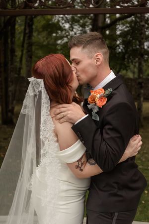 Romantic wedding moment captured outdoors with bride in white dress and flowing veil.