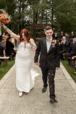A wedding couple walks down a stone path while guests toss orange and pink flower petals in celebration.