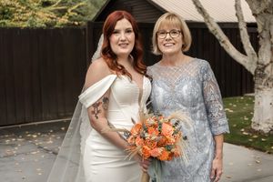 A bride in white holding coral flowers poses with guests at an outdoor wedding venue.