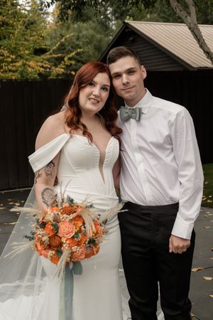 A couple poses with orange floral bouquet during their autumn wedding.