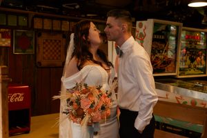 Couple sharing intimate moment with coral bouquet in vintage-styled indoor setting.