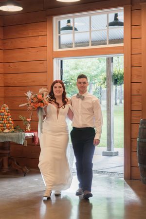 A newlywed couple dances in a rustic wooden venue with large windows and natural lighting.