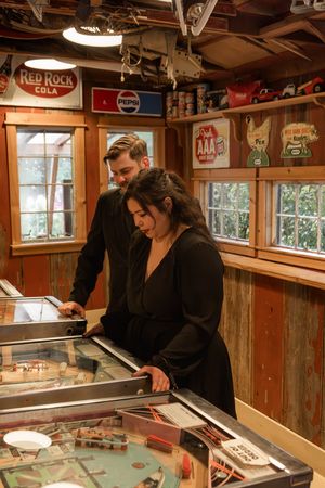 People playing pinball machines in rustic game room with vintage decor.