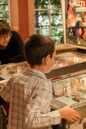 Young boy playing pinball machine in an arcade setting.