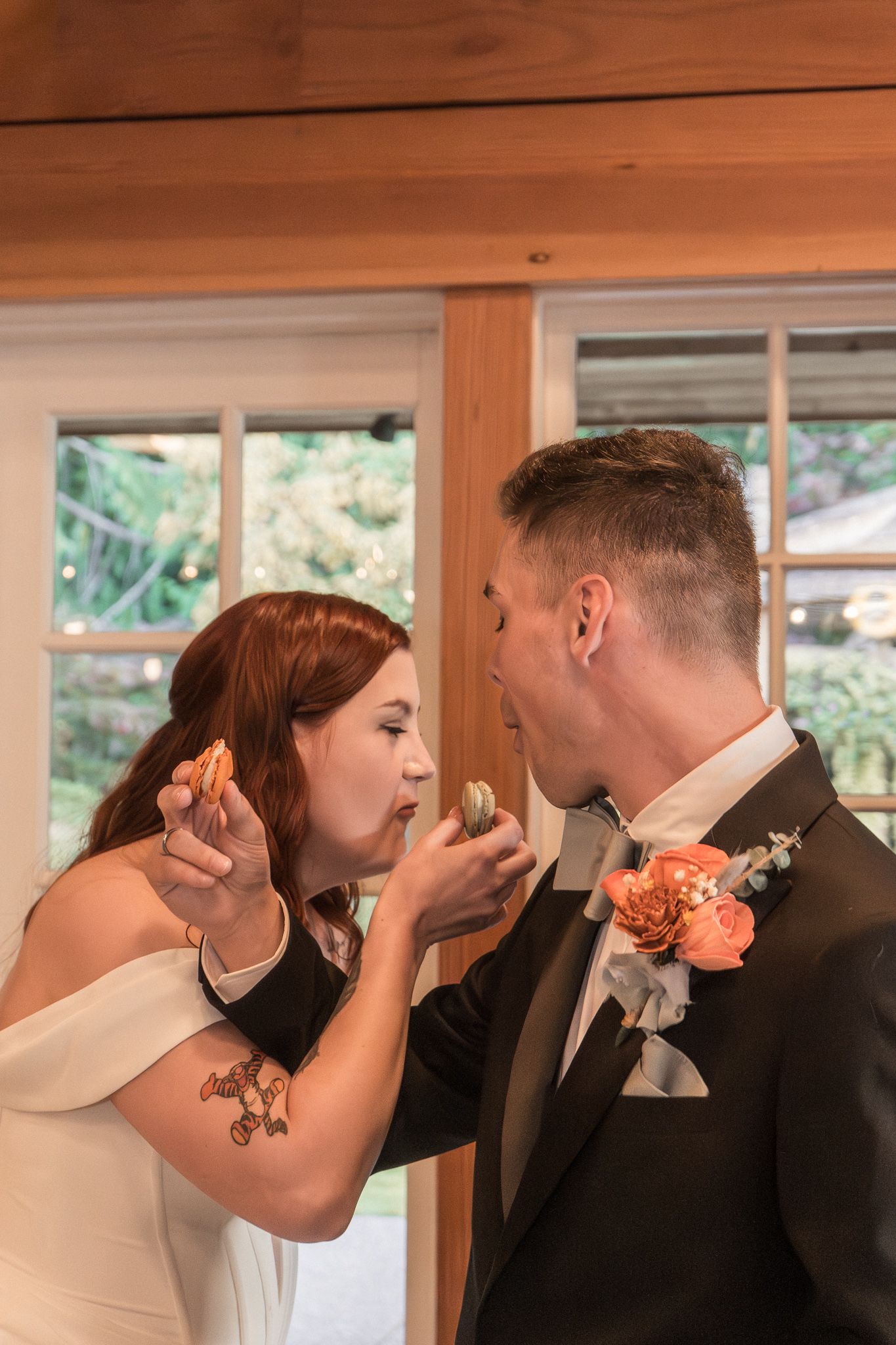 A couple shares their first bite of cake in a rustic wooden venue with natural lighting.