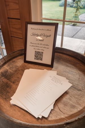 Wedding reception details showing QR code signs and paper cards displayed on a rustic wooden barrel surface.