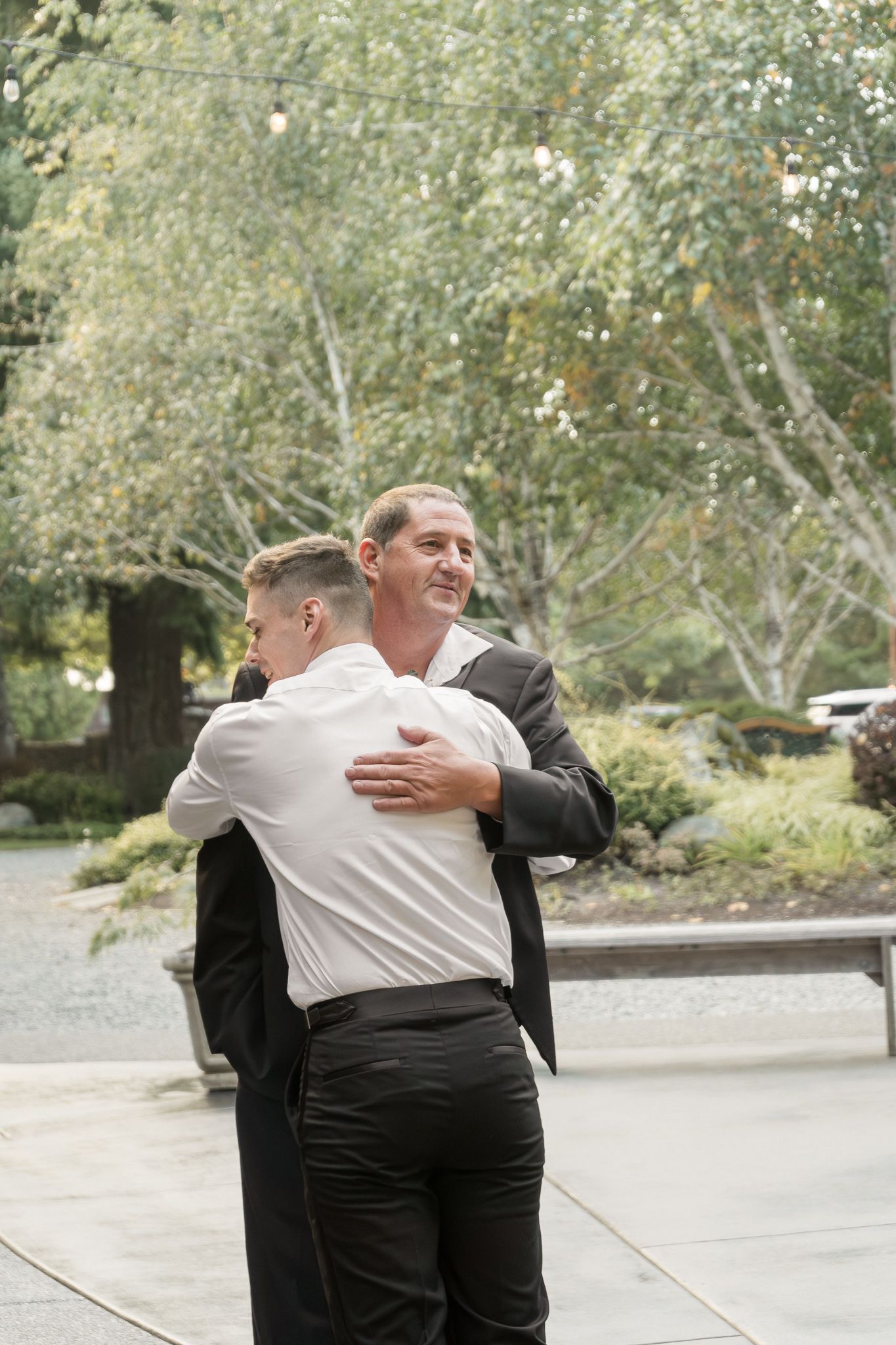 Two people in formal attire sharing an emotional embrace outdoors during a special occasion.