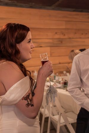 A bride in a white dress sips from a champagne glass during a wedding reception in a rustic wooden venue.