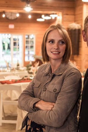 Woman in gray jacket smiles warmly in a rustic wooden interior setting.