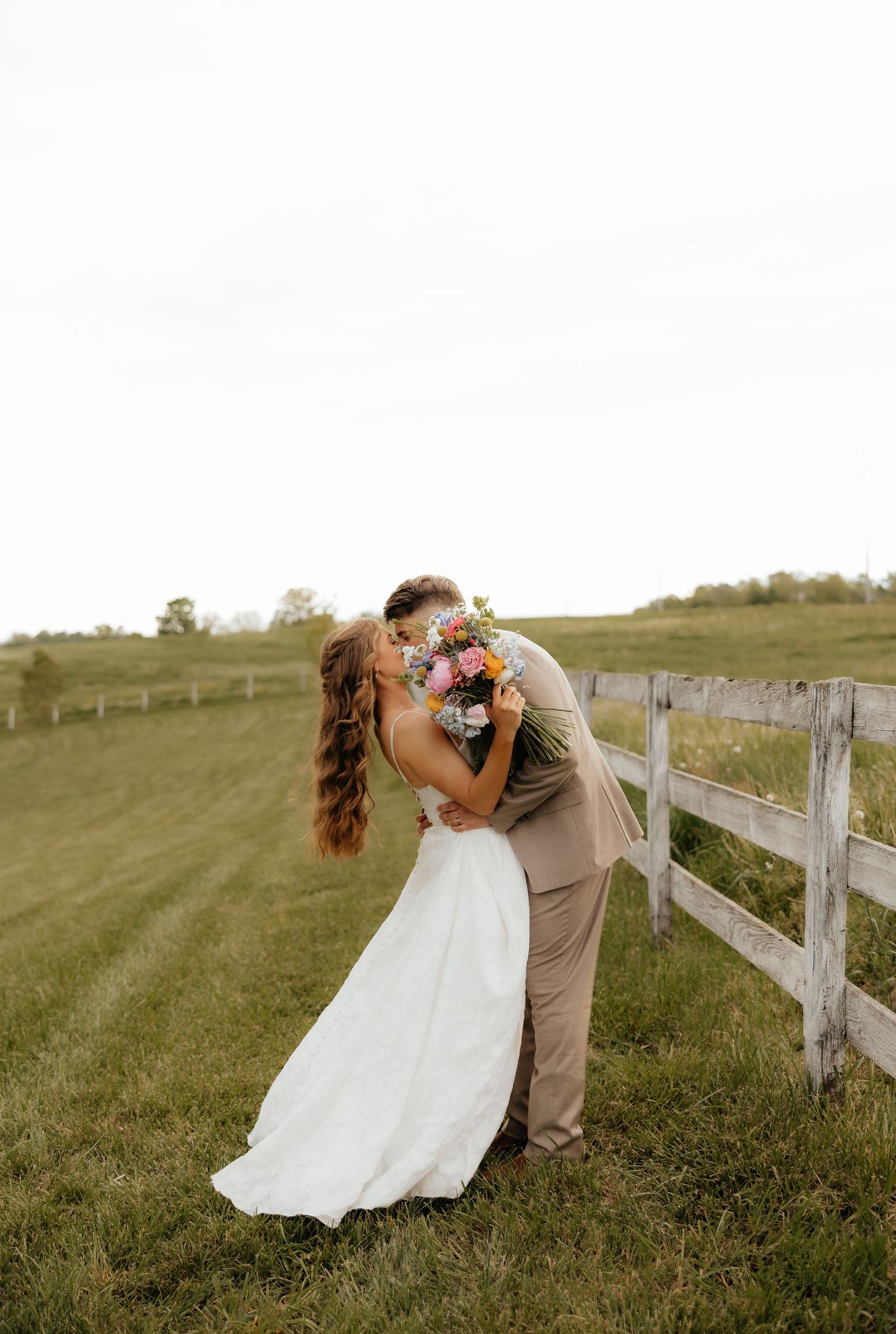 Couple in western wear posing together in green meadow.