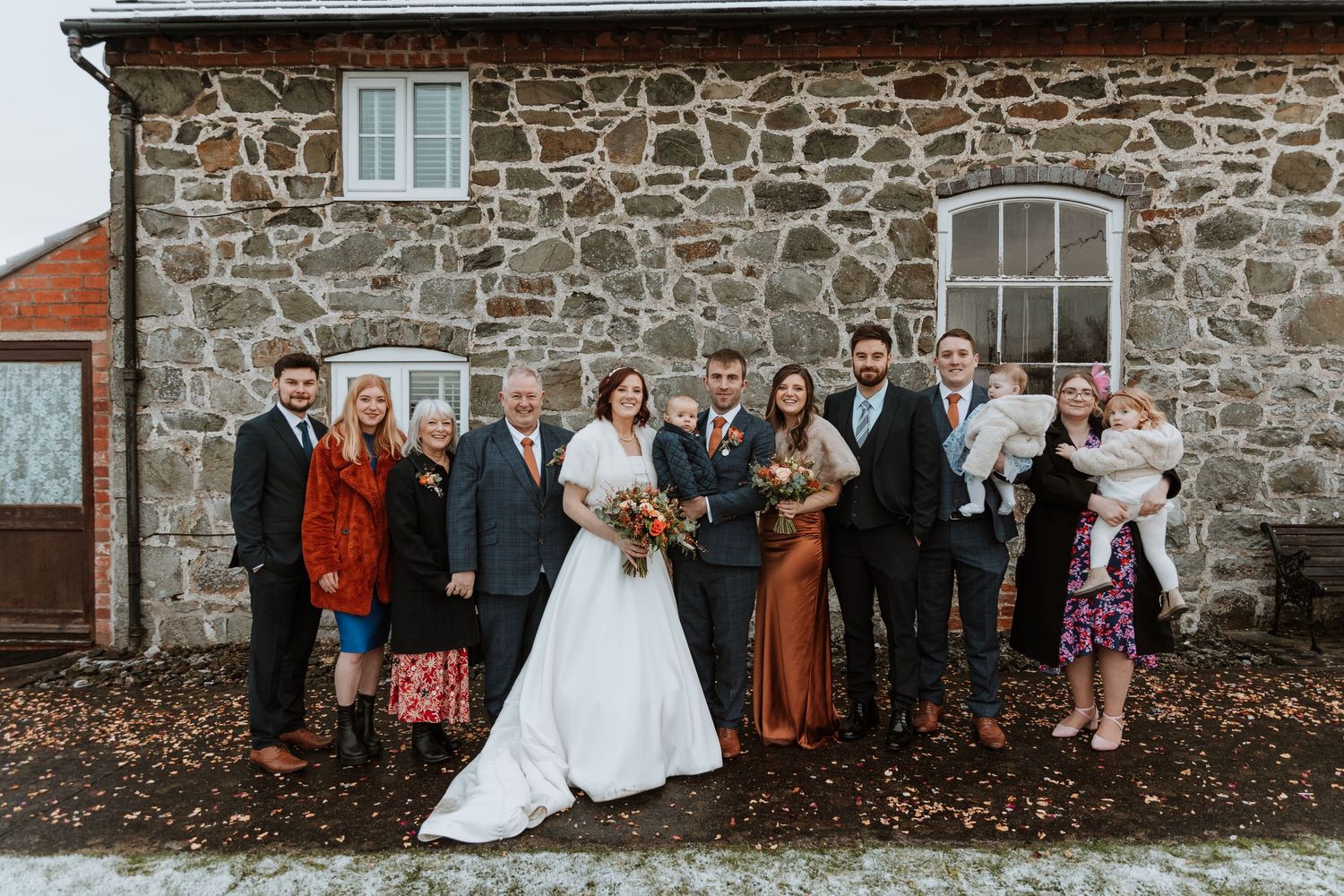 Wedding party poses together against rustic stone wall on autumn day