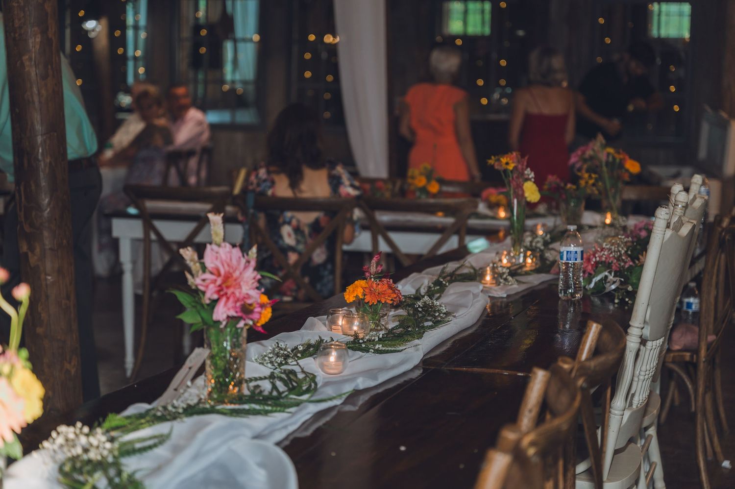 Elegant wedding reception table settings with glowing candles and floral centerpieces in a dimly lit venue.