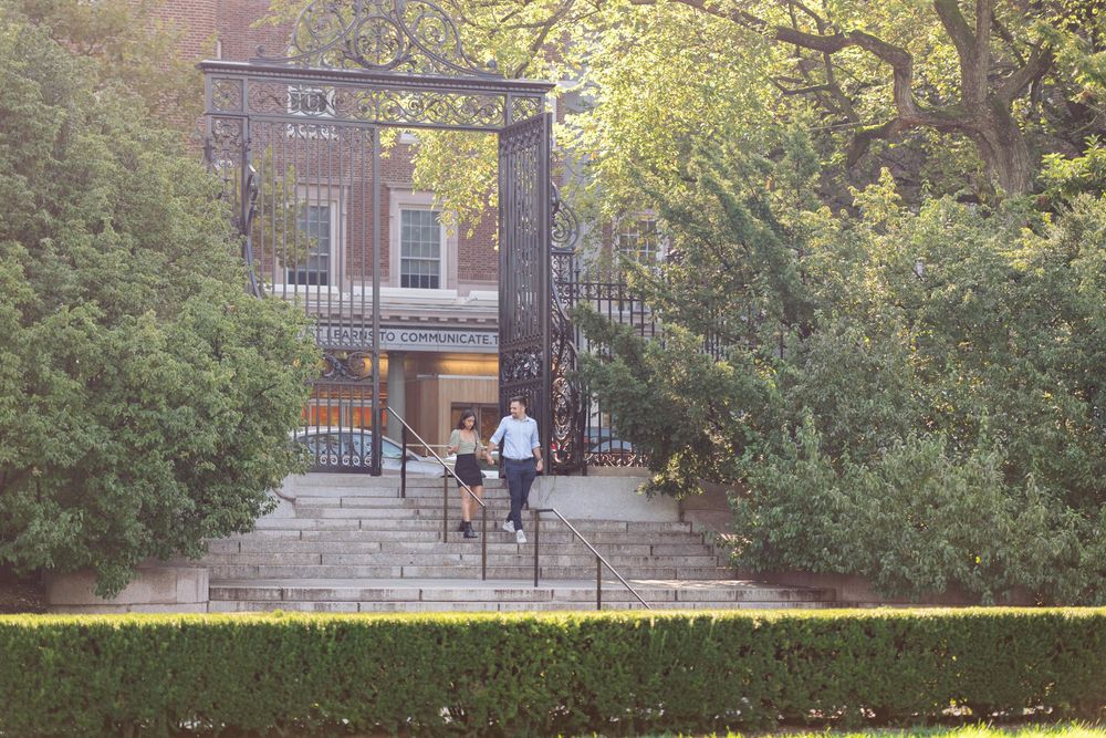 A scenic view of a park pathway with trees and buildings in the background.