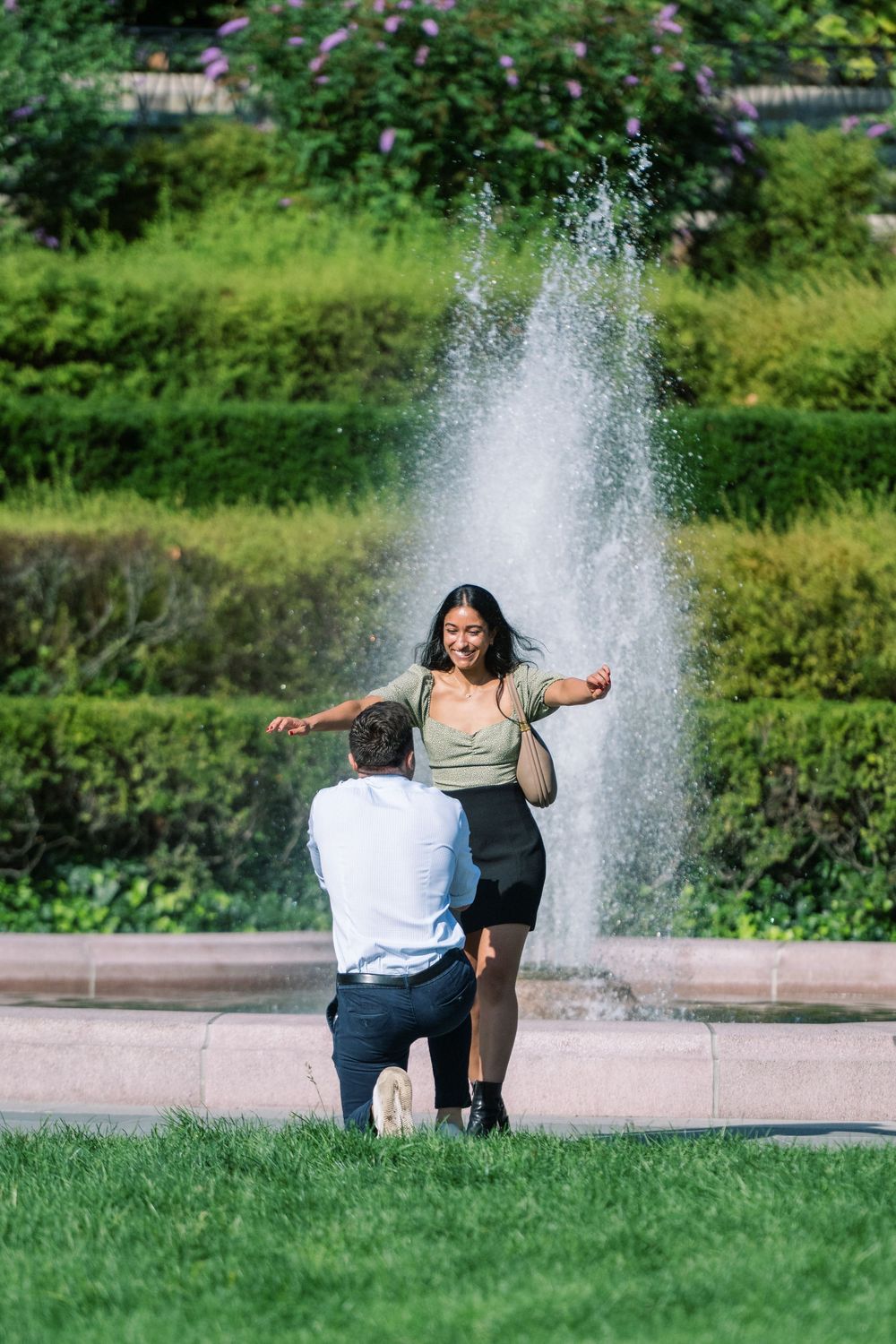 A couple shares a romantic moment near a fountain in a lush green park setting surprise proposal in conservatory gardens central park.
