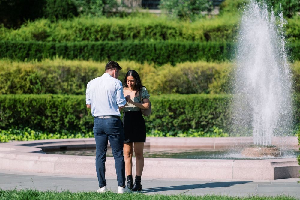 A couple enjoying a special moment near a fountain in a park landscape.
