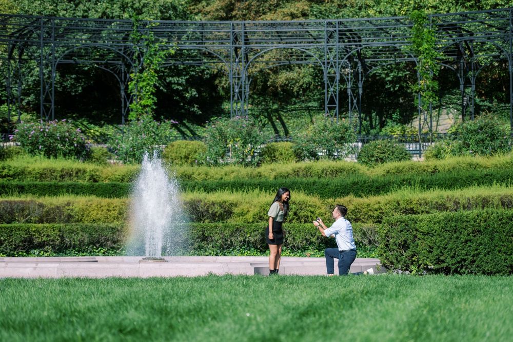 A wide landscape view of a park with a fountain and two people in the distance in conservatory gardens central park.