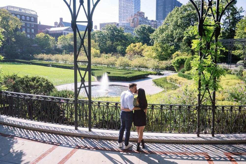 Romantic outdoor photoshoot along a railing with urban skyline and greenery in the background in conservatory gardens central park.