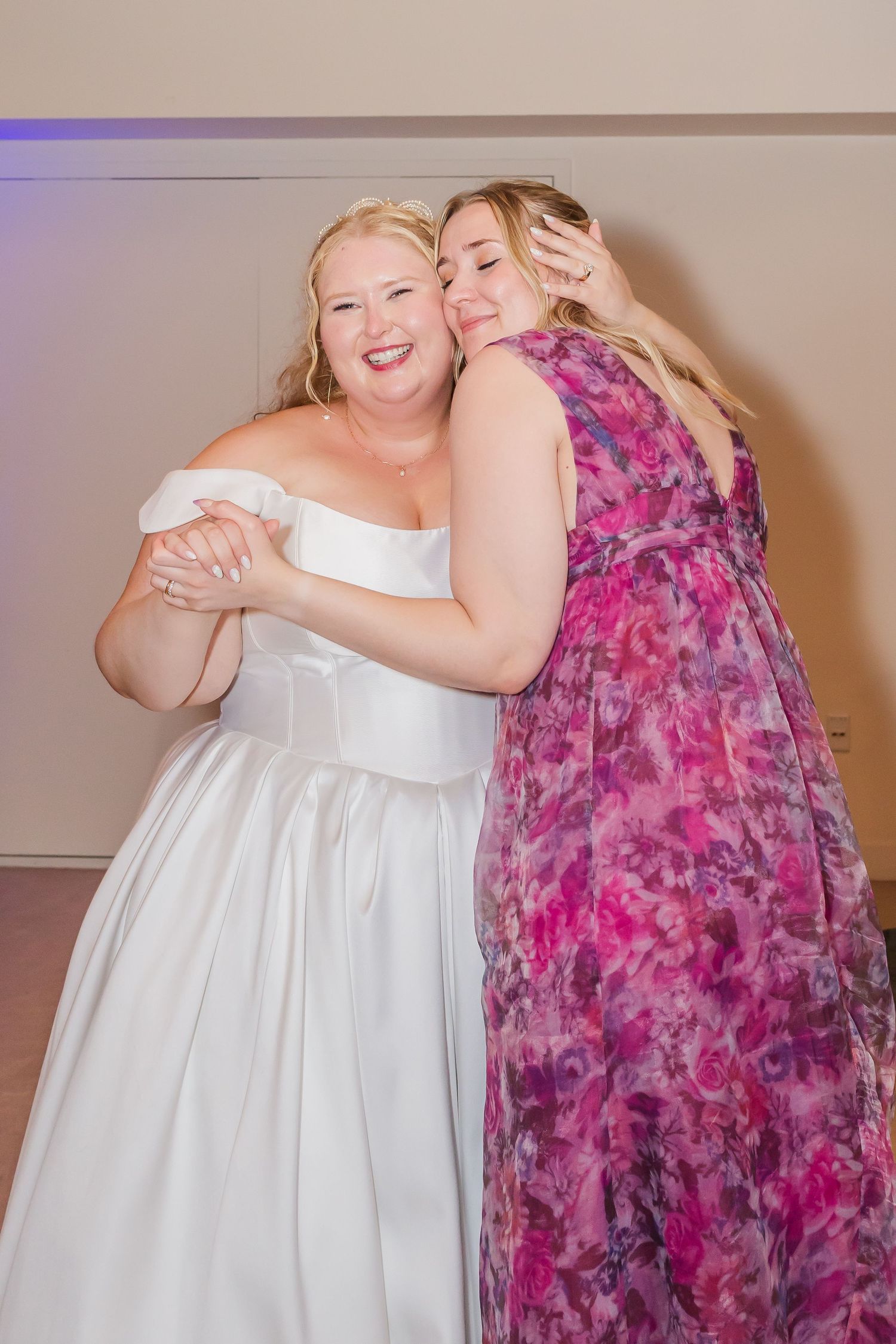 Two people embrace while wearing contrasting white and pink floral dresses at a formal event.
