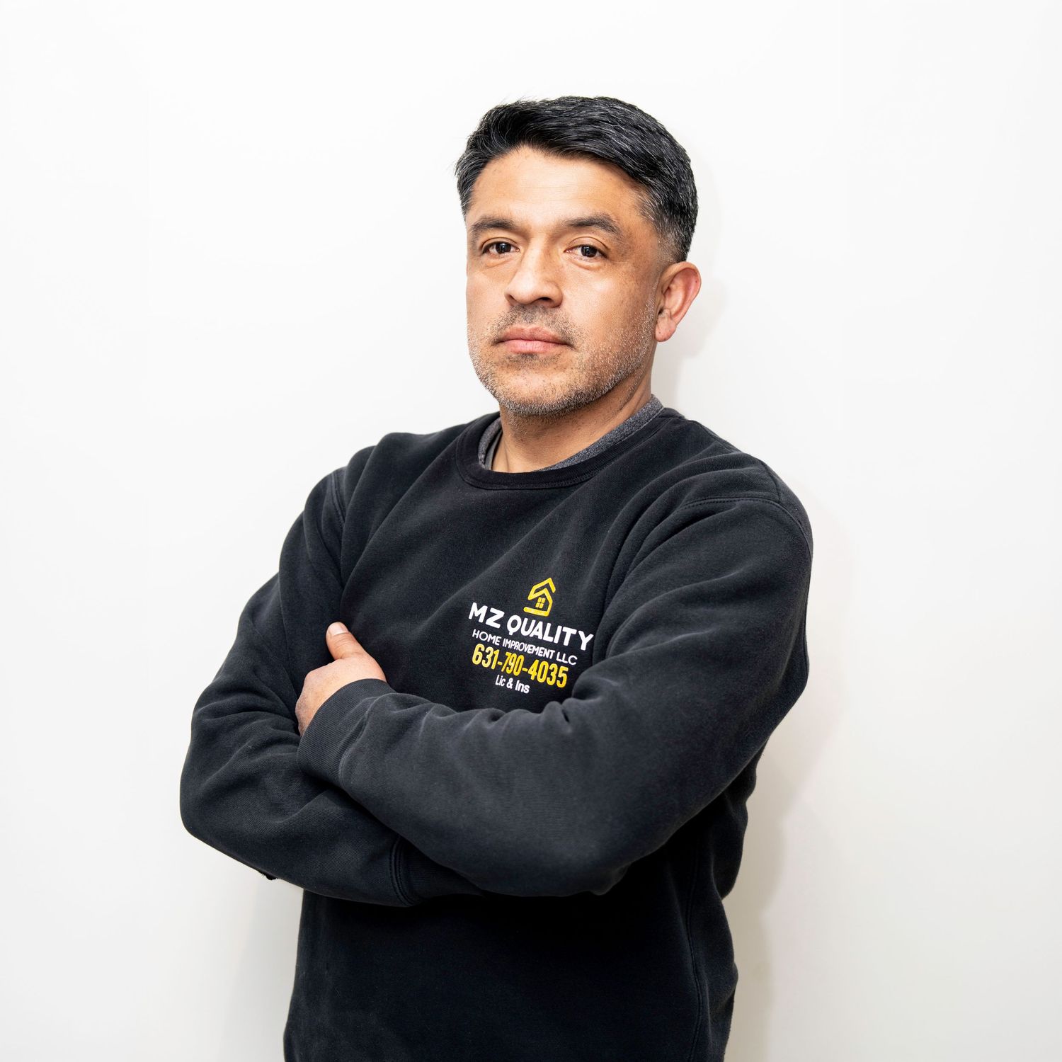 Person wearing a black sweatshirt with NZ Quality text logo standing against white background with arms crossed.