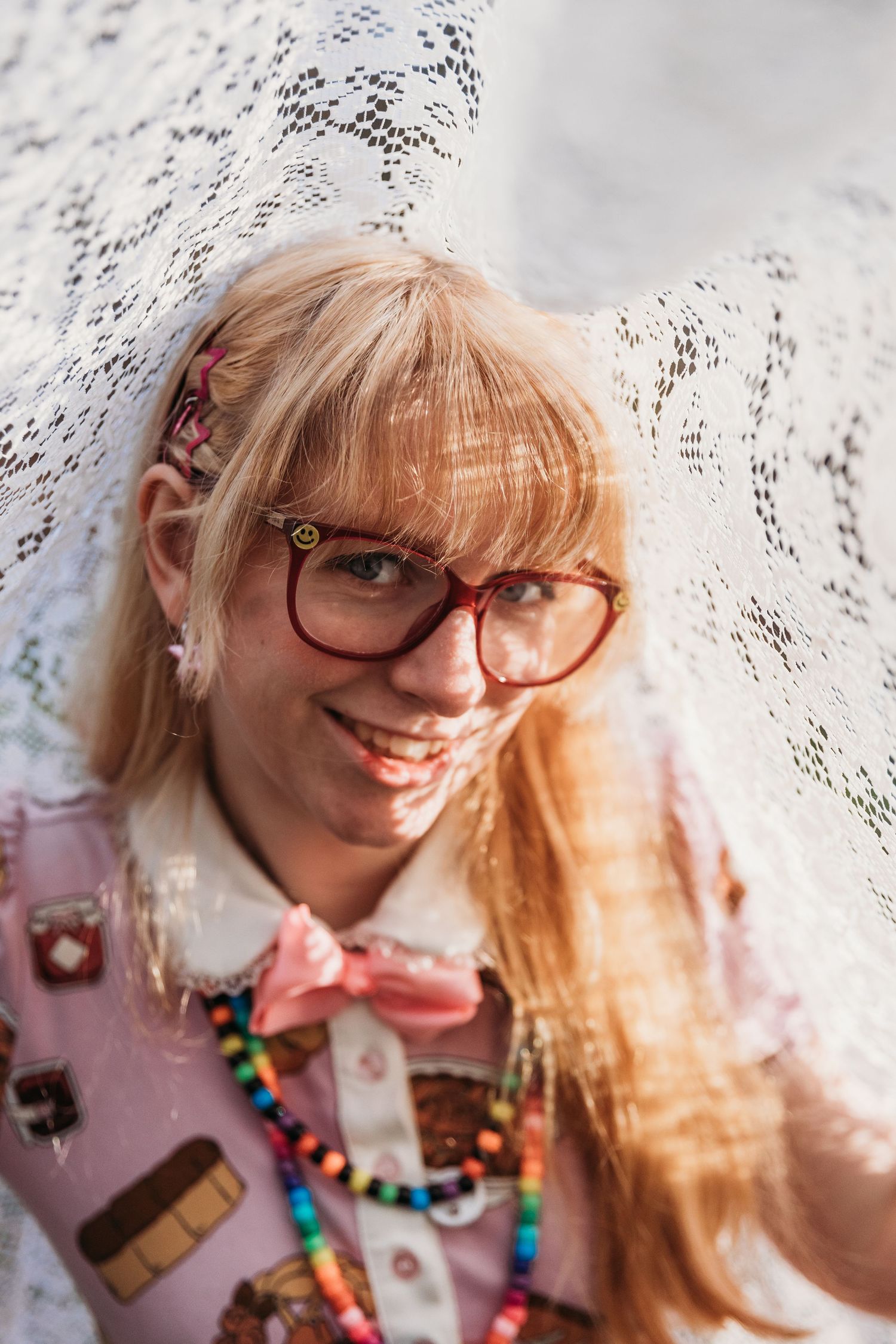 A person wearing glasses and colorful beaded necklaces smiles in a series of four progressive close-up shots.