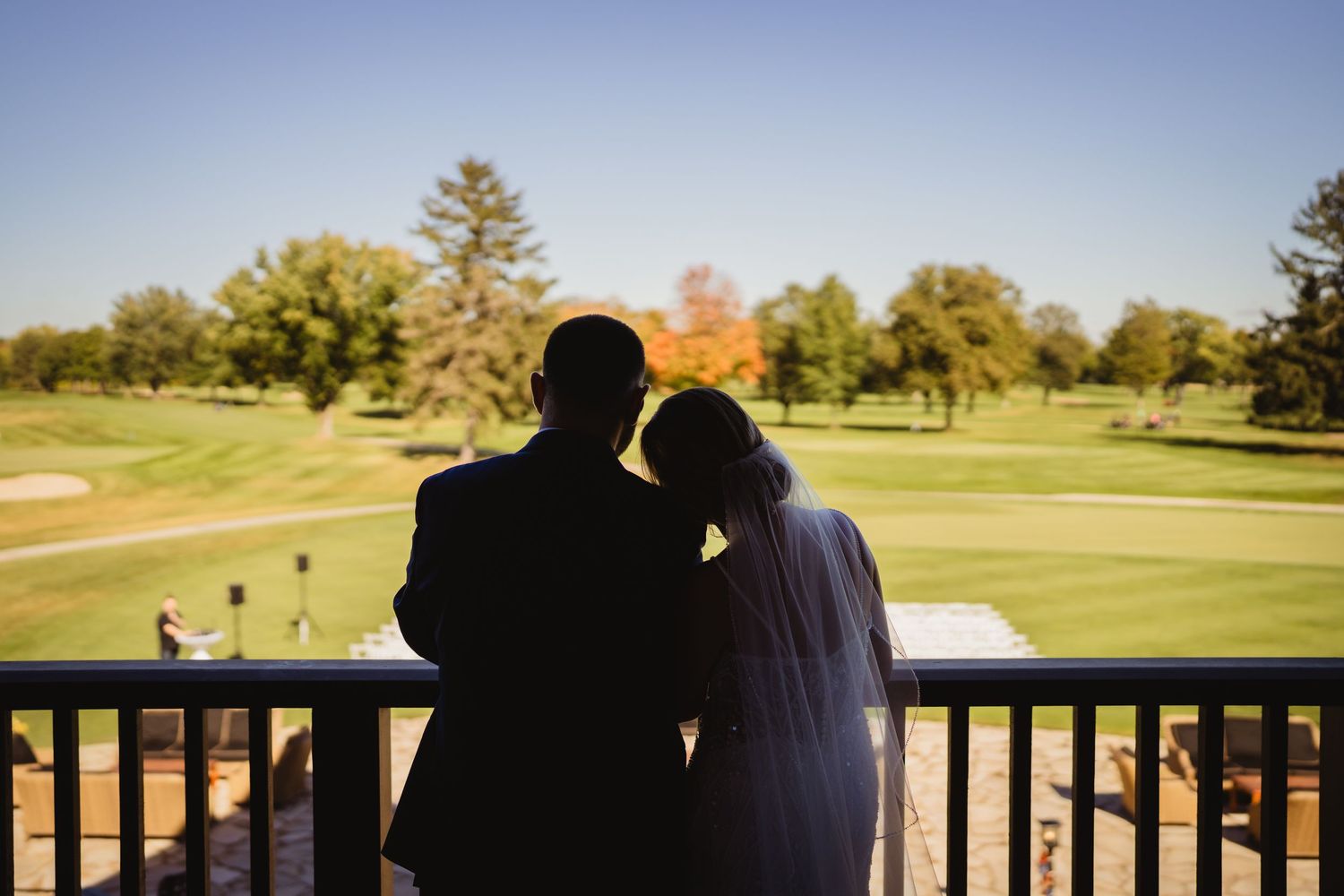 Couple enjoying a romantic moment on a wooden deck overlooking a scenic golf course at sunset.
