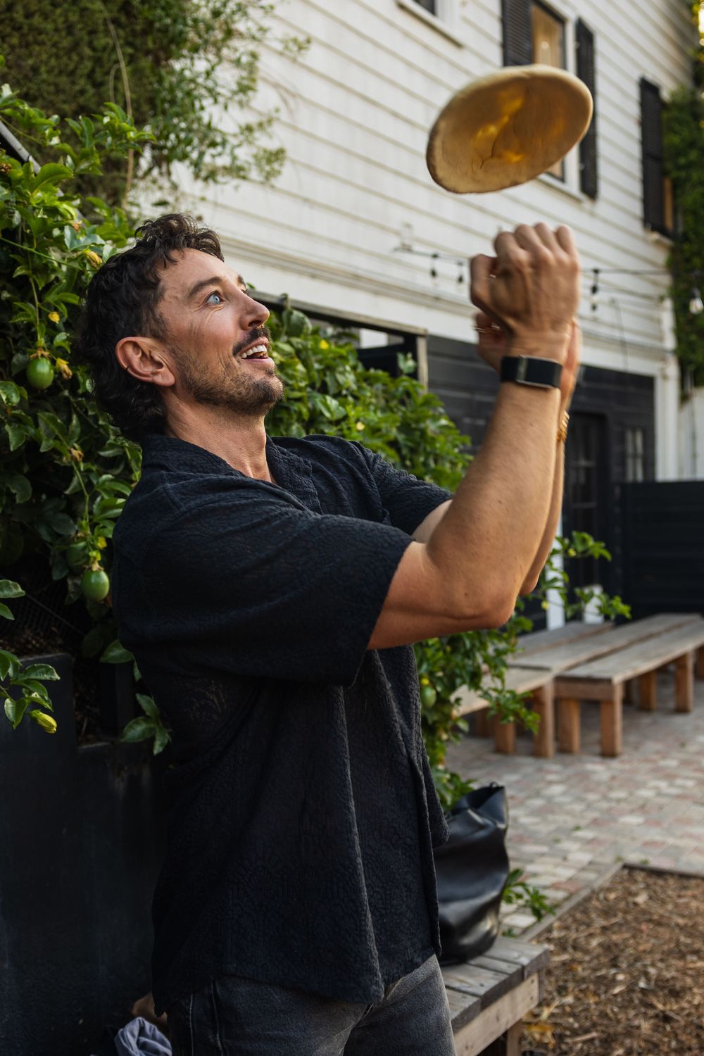 Person tossing pizza dough in the air against white building exterior.