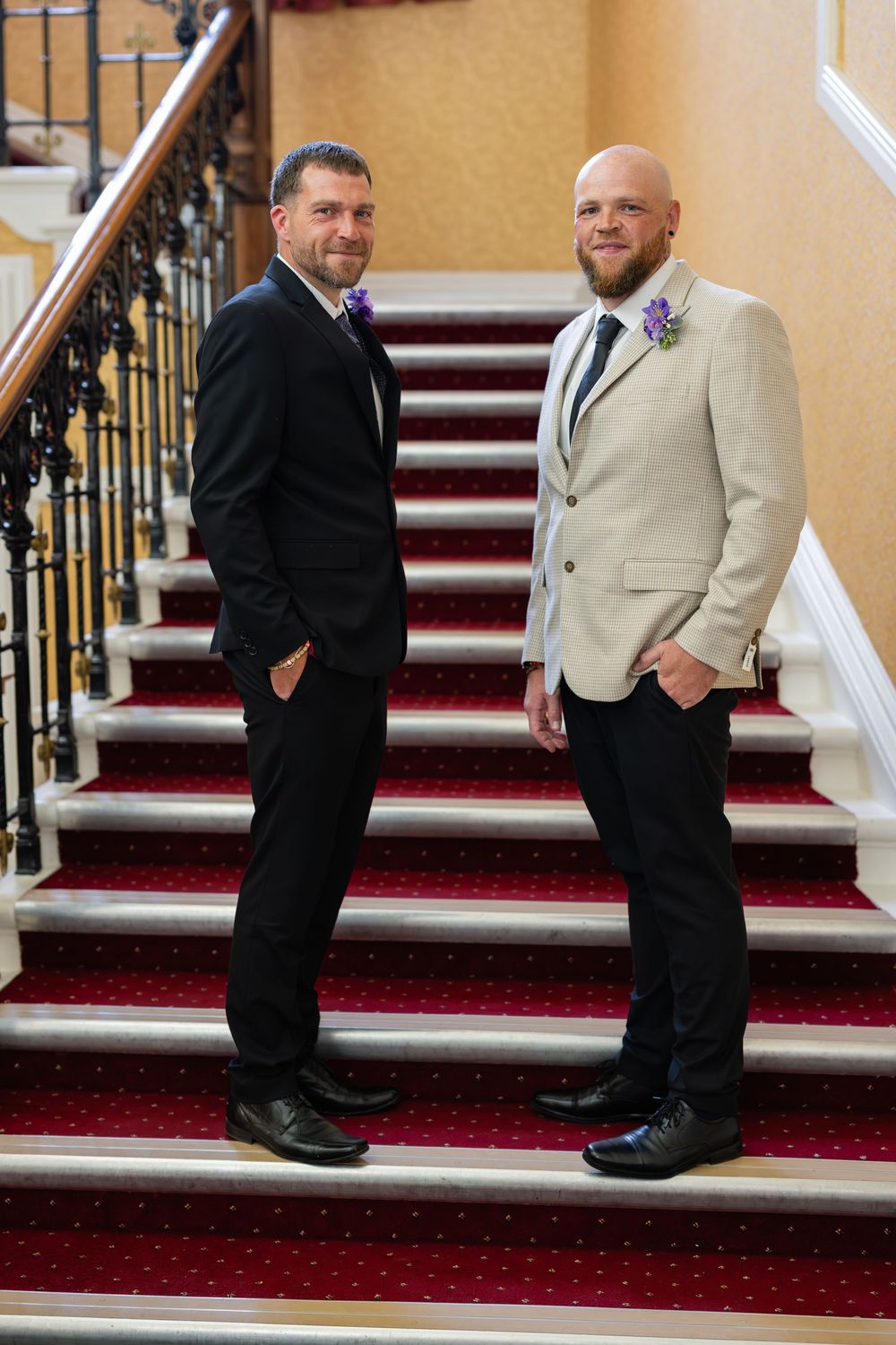 Men in formal attire stand on red carpeted stairs having a conversation.