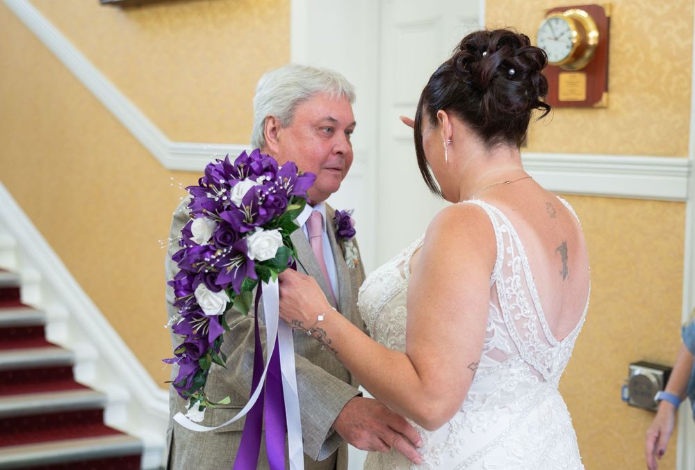 A bride holding a purple bouquet stands on elegant stairs in a white wedding gown.