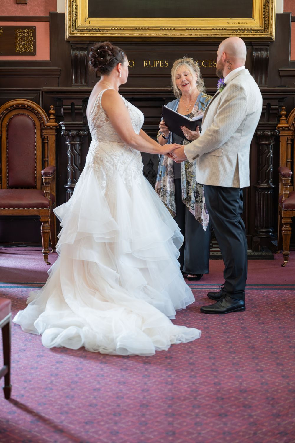 Wedding ceremony taking place in an elegant room with ornate decor and red carpeting.