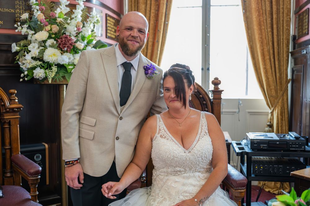 Newlyweds share a joyful moment in an elegant indoor setting with golden curtains.
