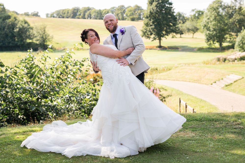 Romantic outdoor wedding photo with couple dancing in sunlit garden setting.