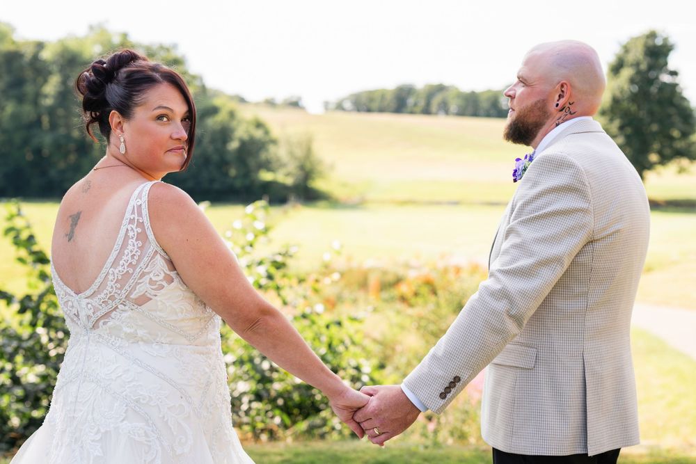 Couple holding hands in scenic outdoor wedding setting with rolling hills in background.