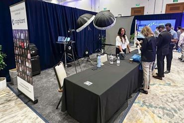 A series of black-draped vendor tables and displays set up at a professional headshot booth during a convention.