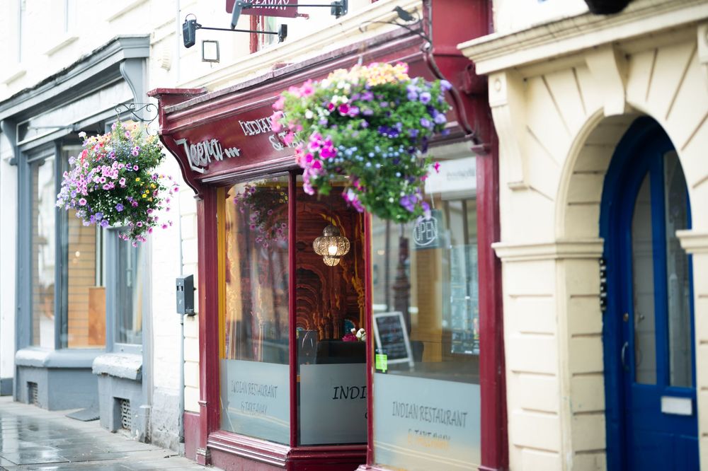 Charming storefront with burgundy trim and hanging purple flower baskets on a quaint street.