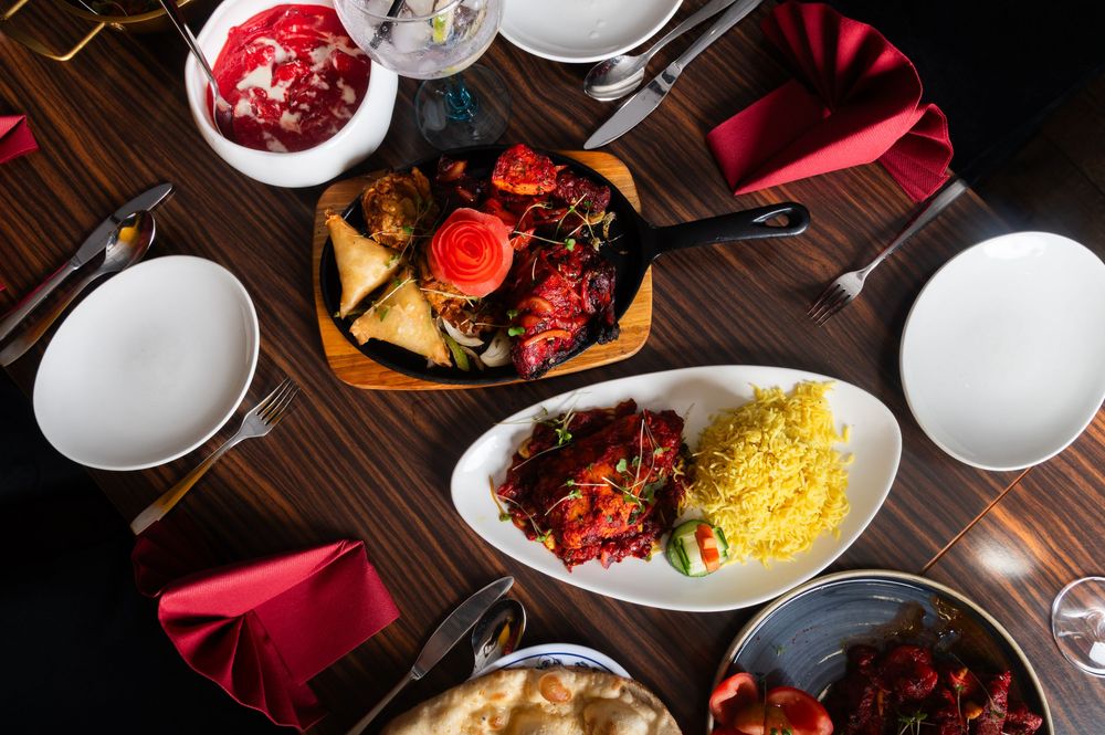 Overhead view of a dinner table with plates of yellow rice, meat dishes, and red napkins on a dark wooden surface.