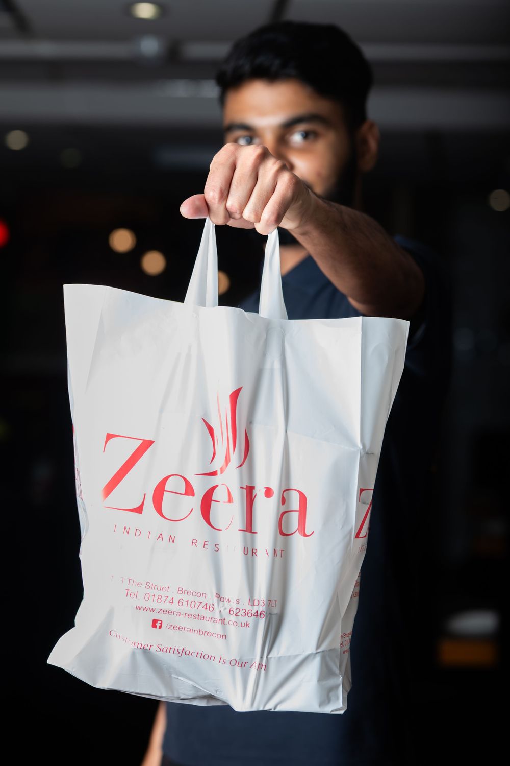 Someone holds up a white shopping bag with red Zeera branding text against a dark background.