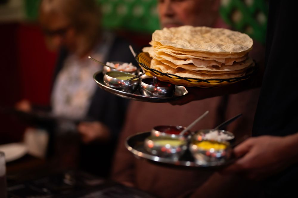 Stack of fresh flatbreads on a serving platter with blurred restaurant setting in background.
