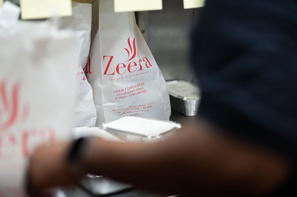 A row of white takeout food containers with red lettering sits on a dark surface.