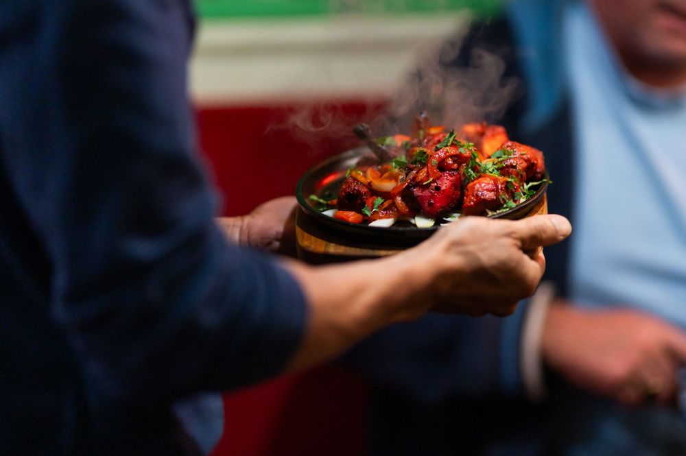 A hand holds a plate of colorful bruschetta topped with tomatoes, herbs and balsamic glaze.